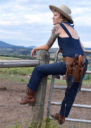 Woman leaning on fence wearing leather toolbelt